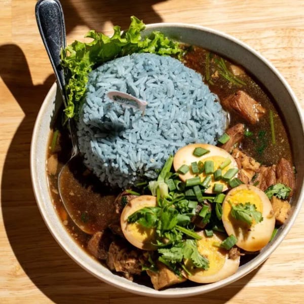 Kin Dee Thai's blue rice with stewed pork, hard-boiled eggs, and fresh herbs in a bowl.