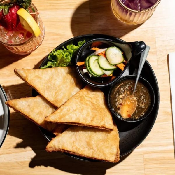 Crispy golden fried wontons with a side of pickled vegetables and dipping sauce, alongside cocktails.