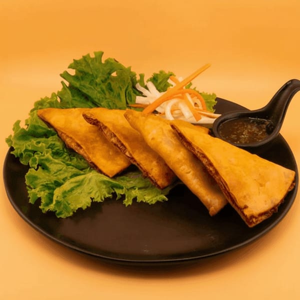 Golden fried spring rolls with lettuce, shredded carrots, and dipping sauce on a black plate.