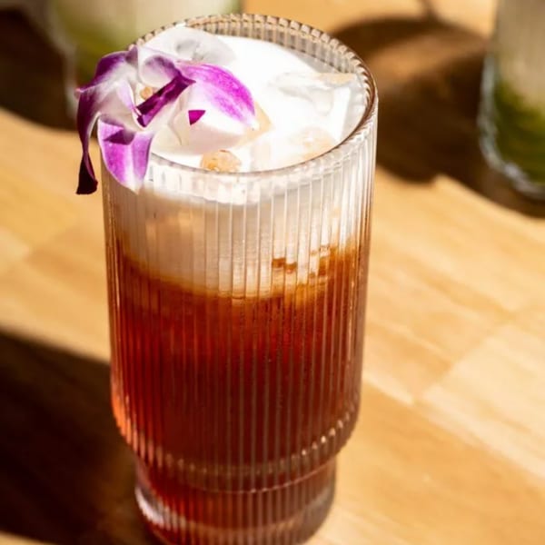 Kin Dee Thai iced tea with a creamy top, ice, and a purple orchid garnish.
