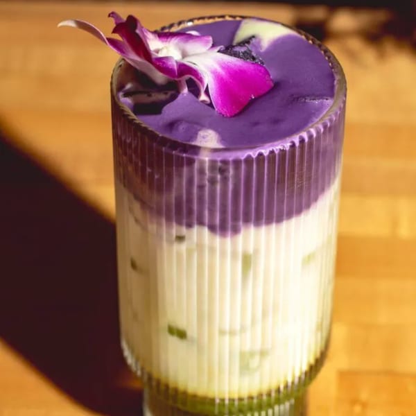 A vibrant purple and white layered drink in a textured glass, garnished with a pink orchid.